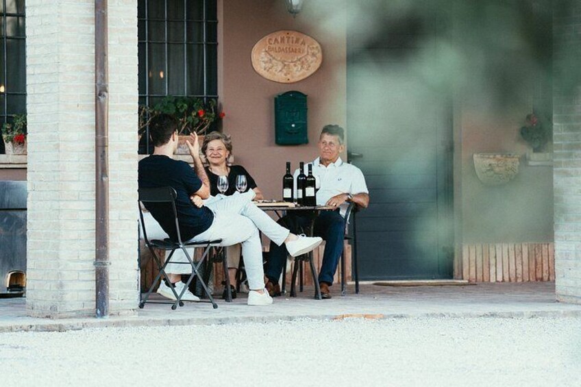 A group of people sitting at an outdoor table with drinks, a brick building, and a sign with a circular design. 3