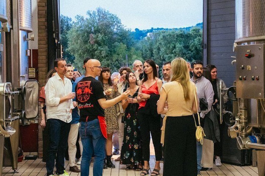 A group of people standing in a brewery with large brewing equipment in the background. 2