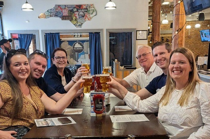 A group of people toasting with beer glasses at a bar with a map on the wall. 1