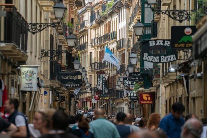 A crowded street lined with buildings, street lamps, and various signs, including a flag. 3