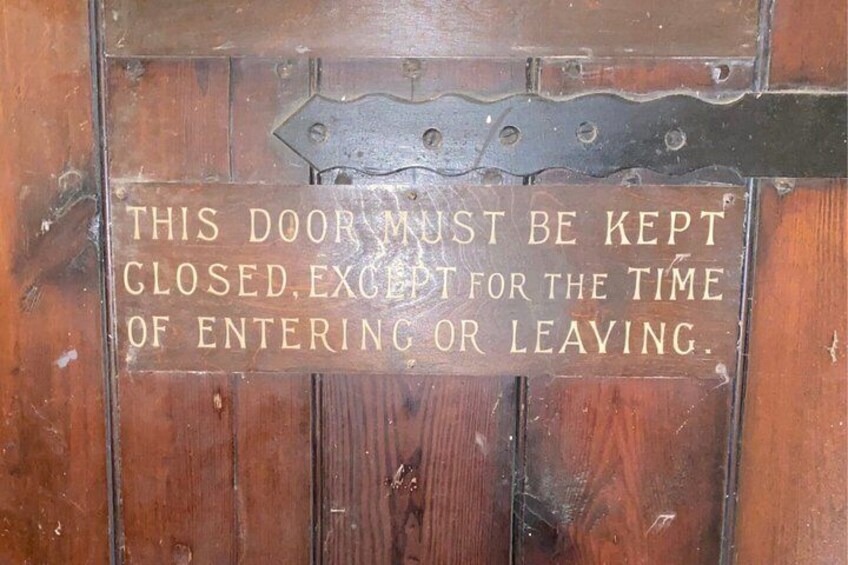 A wooden door with a metal latch and a sign that reads 'THIS DOOR MUST BE KEPT CLOSED, EXCEPT FOR THE TIME OF ENTERING OR LEAVING.' 5