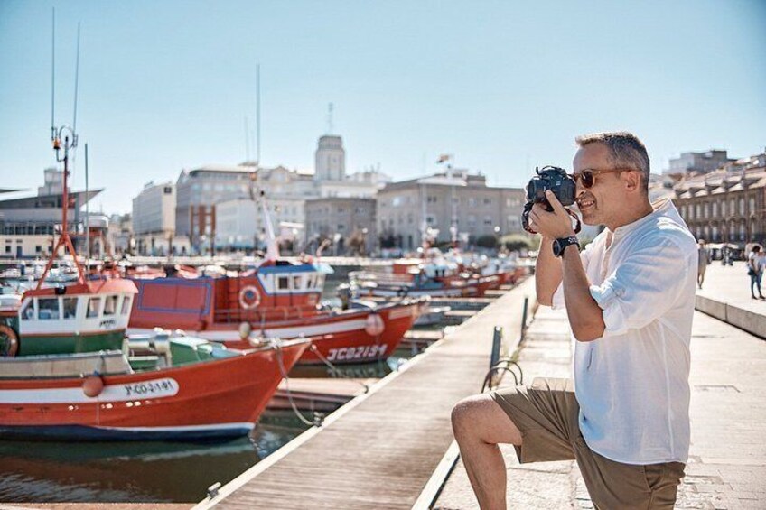 A man taking a photo with a camera, a dock, and several boats in the background. 2