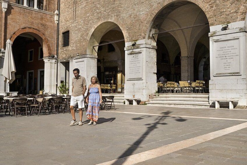 A couple walking in a courtyard with arches and outdoor seating. 2