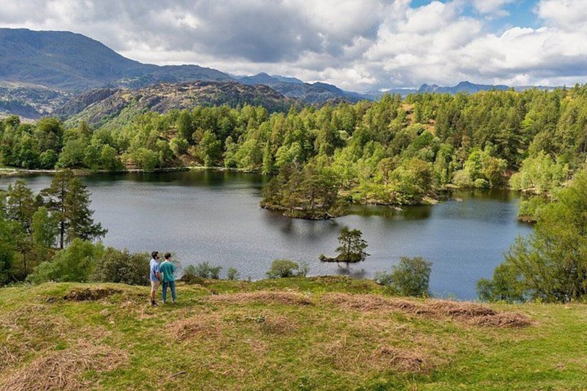 A lake surrounded by forested hills, with two people standing on a grassy area. 5