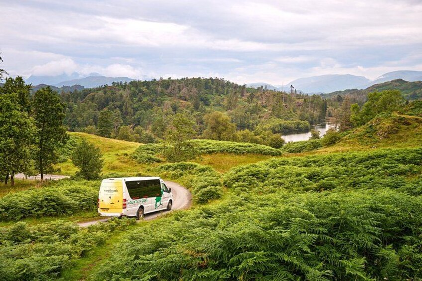 A yellow van on a winding road through a lush green landscape with hills and a river in the distance. 3
