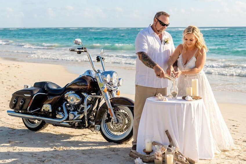 Una boda en la playa con una motocicleta, una mesa con velas y una pareja cortando un pastel. 1
