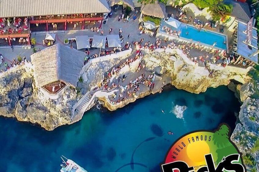 A coastal area with a large crowd, a swimming pool, and a building with a thatched roof. 1