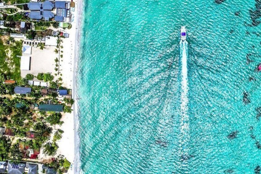 A boat creating a wake in turquoise waters, a beach with buildings and palm trees, and a clear sky. 4