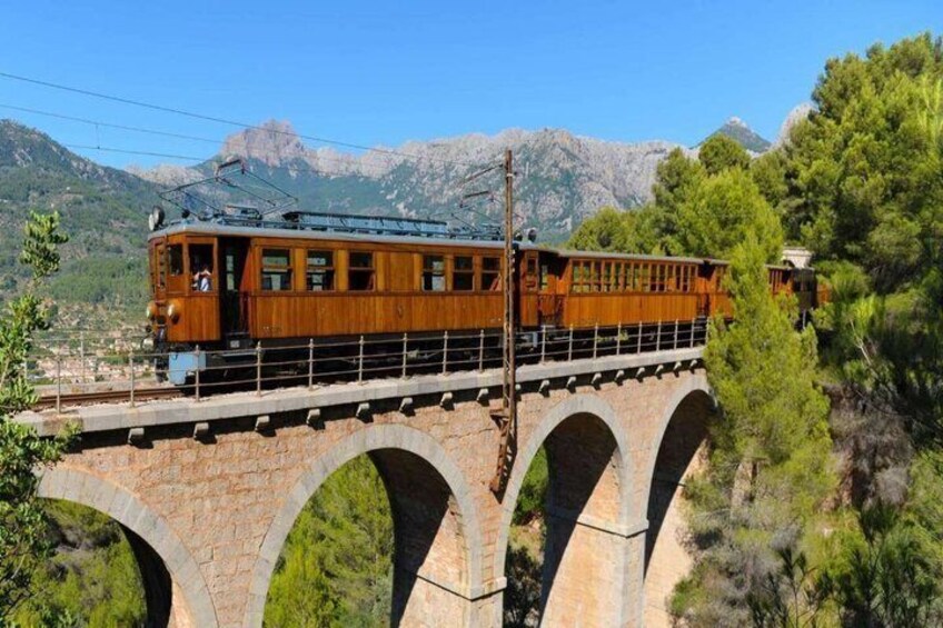A wooden train on a stone bridge with mountains in the background. 2