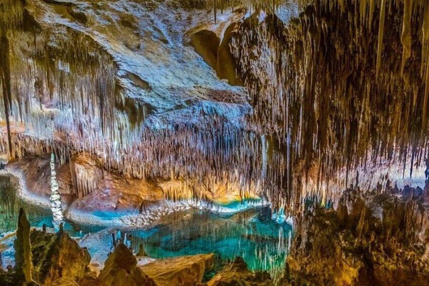A cave with stalactites and stalagmites, a pool of water, and rock formations. 2
