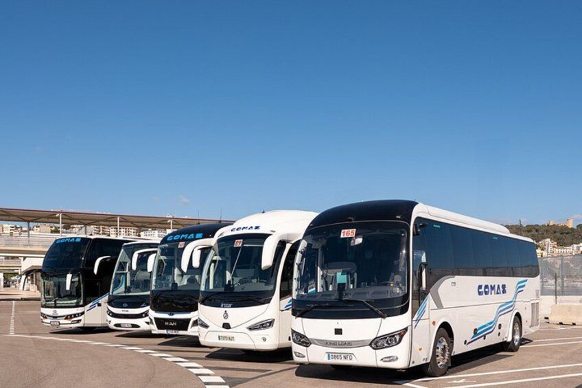 A row of white buses with blue and black accents parked in a lot. 4