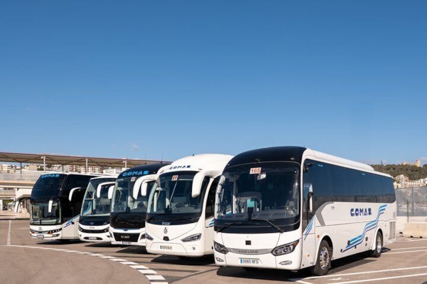 A row of white buses with blue accents parked in a lot. 2