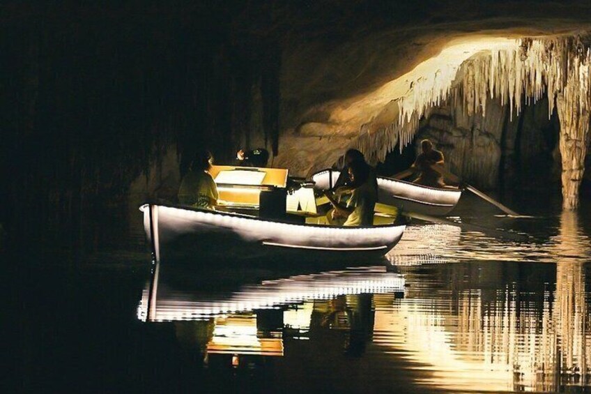 A cave with stalactites, two boats with people, and a calm body of water. 1