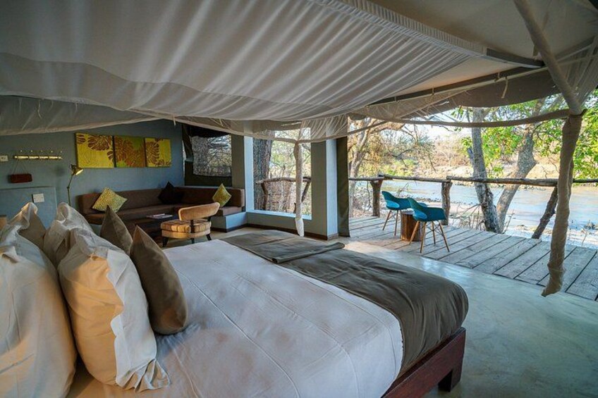 A tented accommodation with a bed, a sofa, and a table with chairs. 5