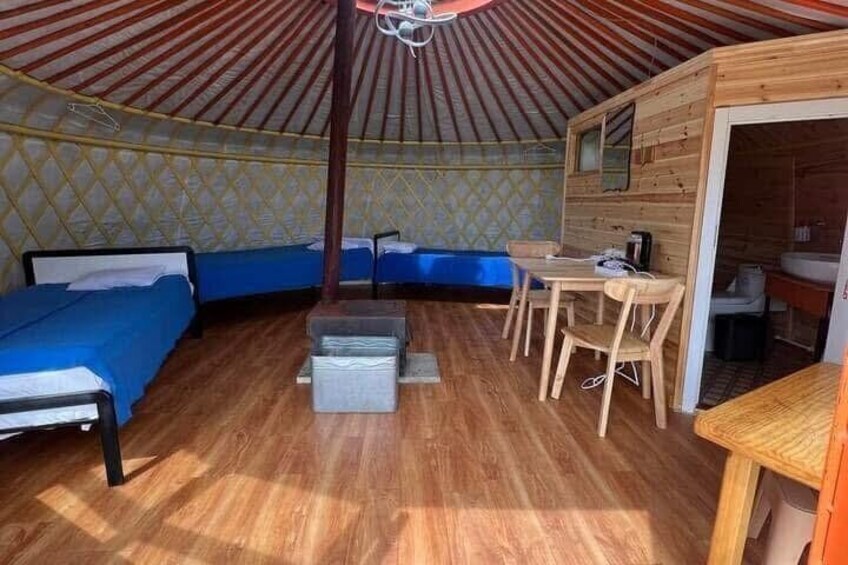 A yurt interior with wooden walls, a central seating area, and a small table. 4