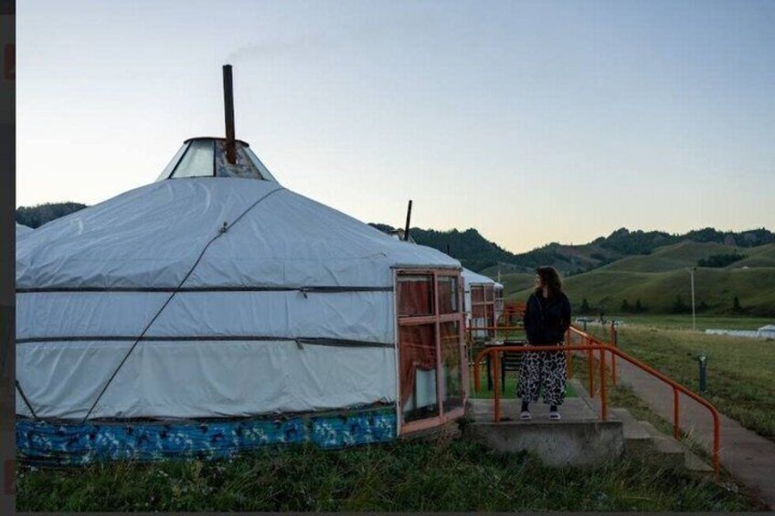 A white yurt with a metal staircase leading up to a door, set in a grassy field with hills in the background. 3
