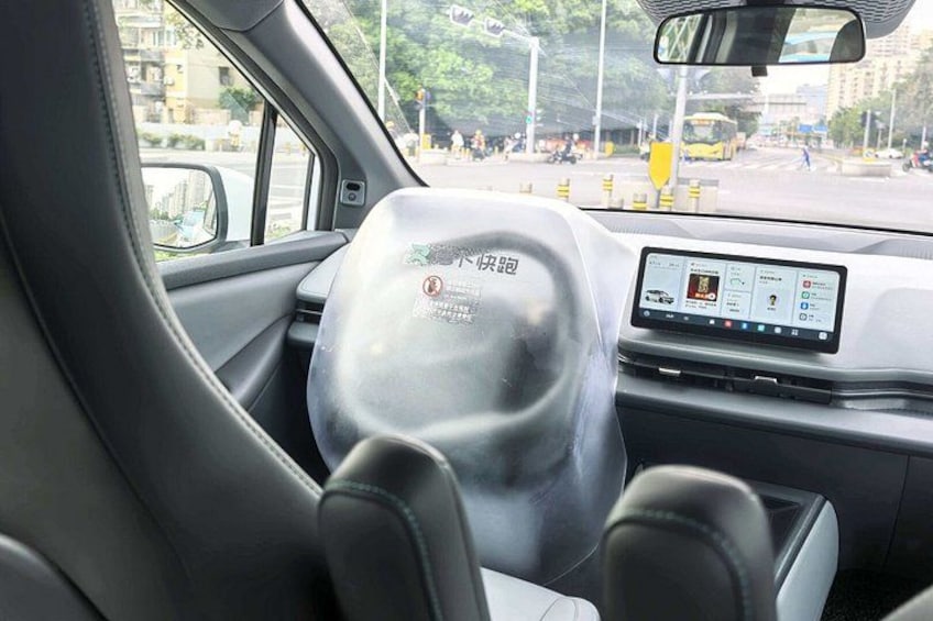 A car interior with a steering wheel, dashboard, and a view of the street outside. 3
