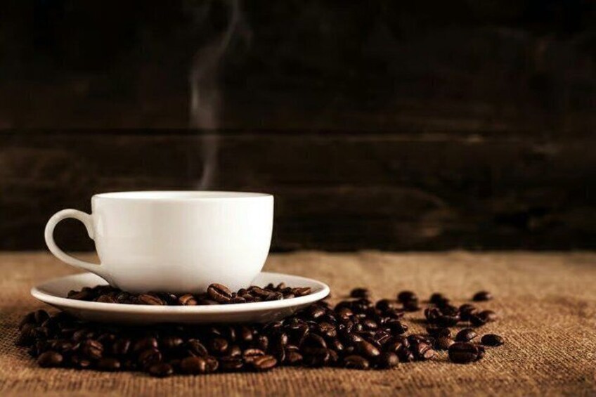 A white cup of coffee on a saucer with coffee beans scattered around it. 4