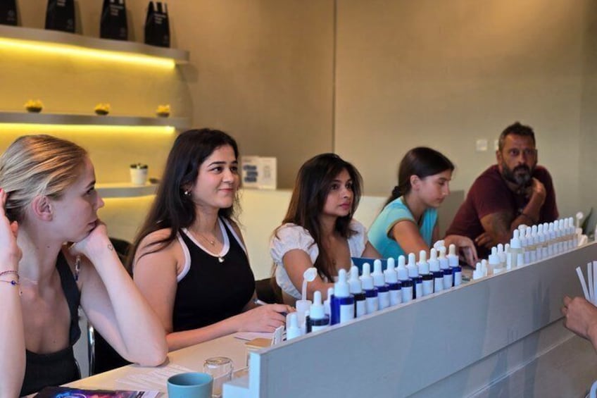A group of people seated at a counter with various items, including bottles and a computer. 5
