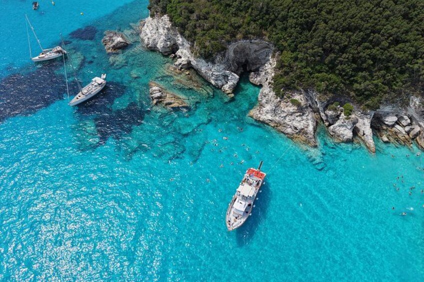 A coastal area with clear turquoise waters, rocky cliffs, and boats anchored near the shore. 1