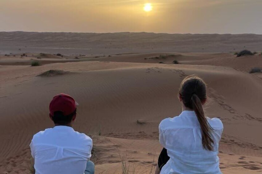 Two people sitting on sand dunes facing the sunset. 4