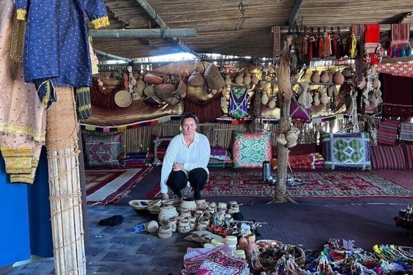 A person in a traditional market with various textiles, pottery, and woven items displayed. 3