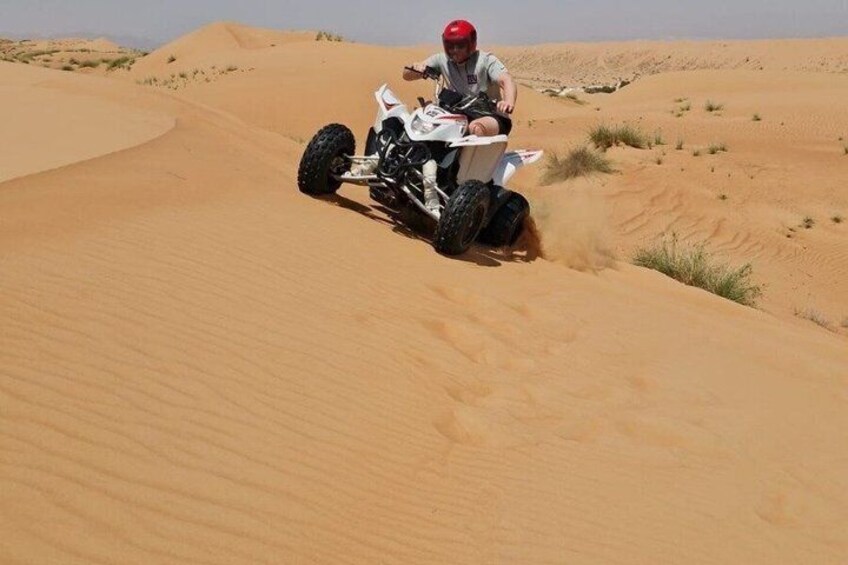 A person riding a white quad bike on a sandy dune. 1