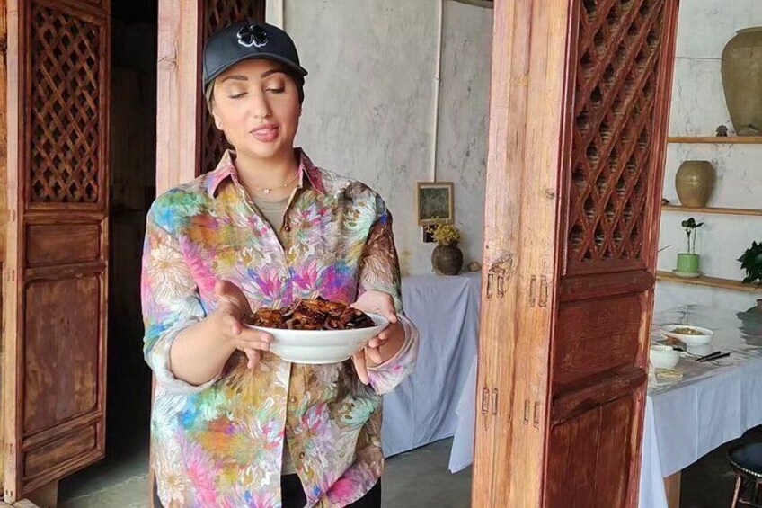 A person holding a plate of food in a room with wooden doors and a table with a vase. 2