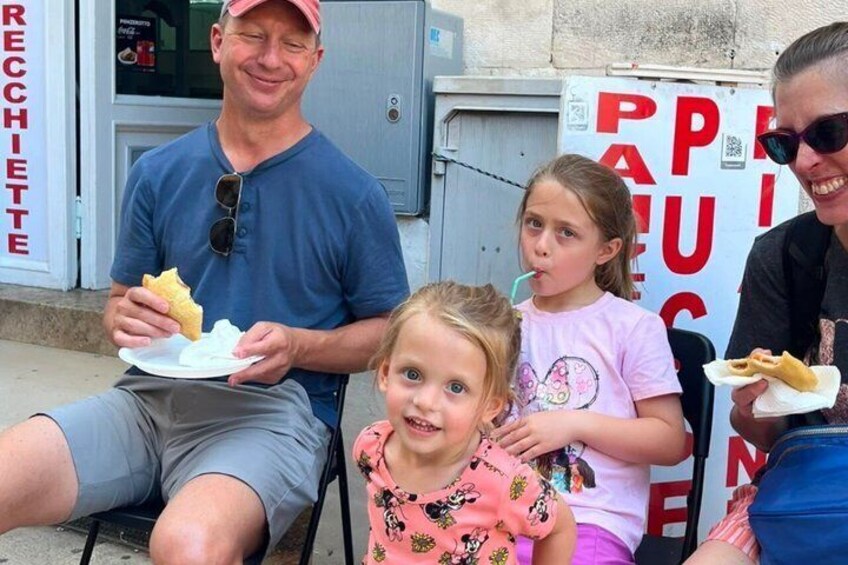 A man and two children sitting at an outdoor table with food. 3