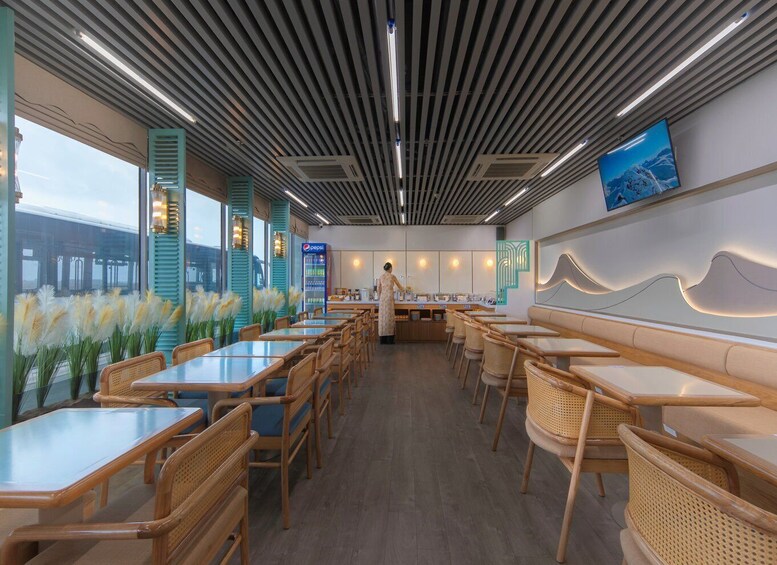 A modern restaurant interior with wooden tables and chairs, a pepsi refrigerator, and a large window overlooking a bridge. 3
