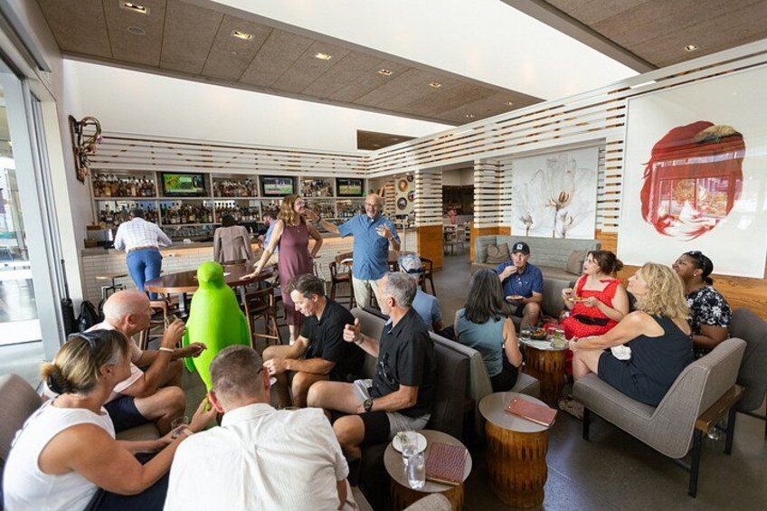 A group of people seated in a modern indoor setting with a bar area in the background. 2