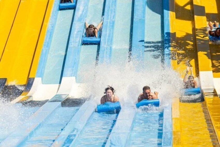 A water slide with multiple lanes, water splashes, and people sliding down. 5