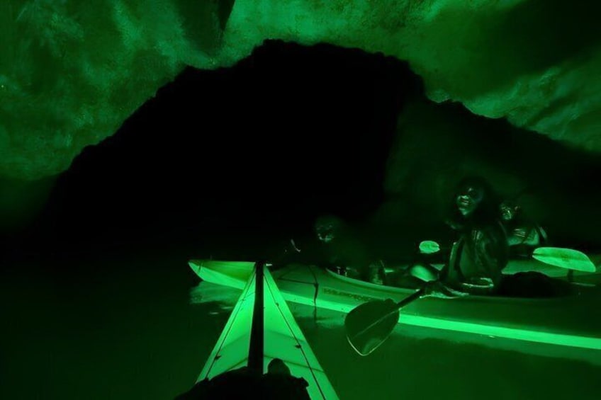 A cave with green lighting, a kayak, and a paddle. 2