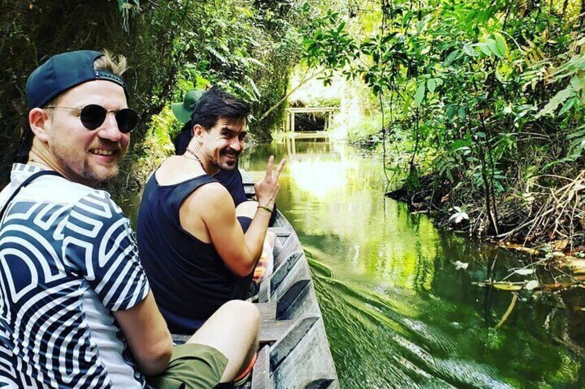 Two people on a narrow waterway surrounded by dense greenery. 1