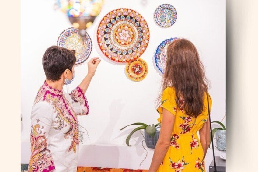 Two people examining decorative plates on a wall. 2