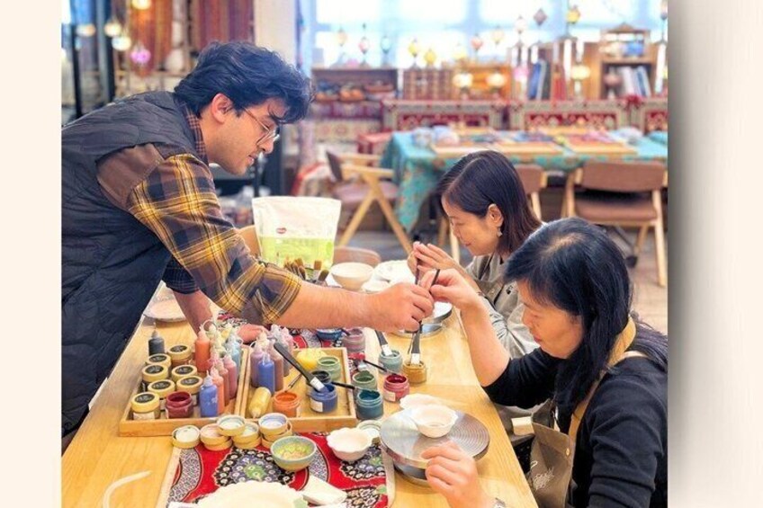 A person painting on a canvas with various art supplies on the table. 3