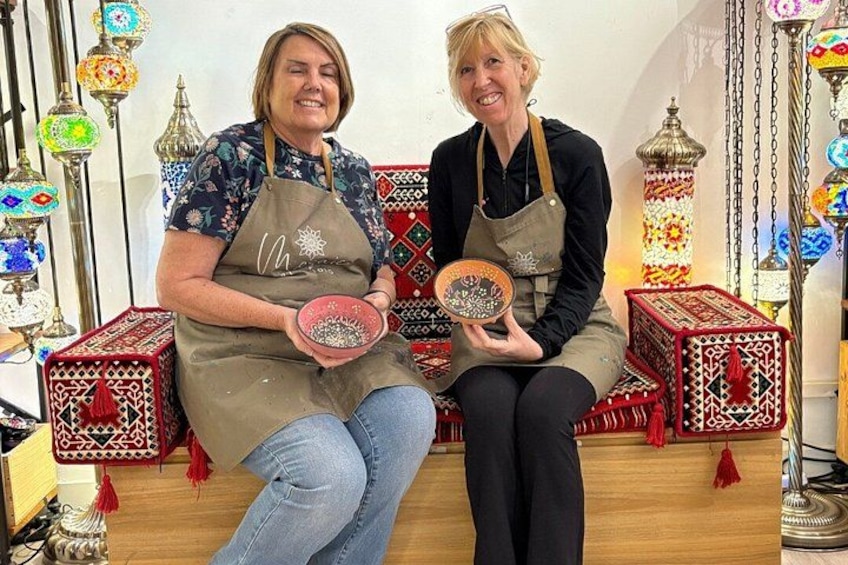 Two individuals seated on a bench, each holding a decorative plate. 4