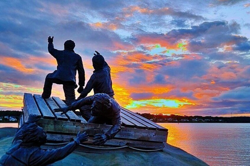 A sunset over a body of water with a sculpture of two figures on a bench. 4