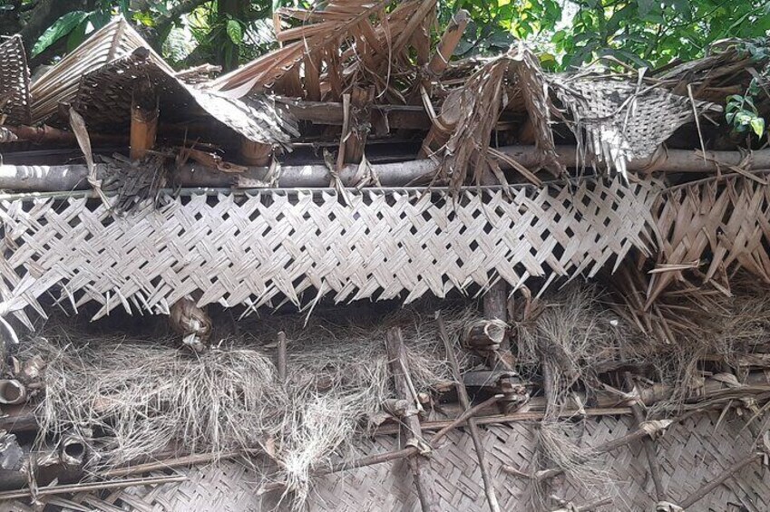 A traditional woven structure with a lattice design, surrounded by natural debris and vegetation. 2