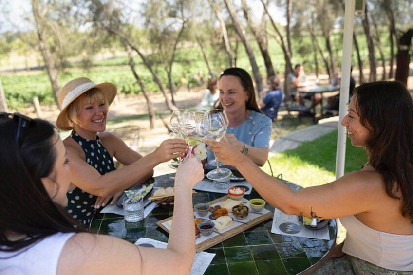 A group of people toasting with wine glasses at an outdoor table with a green tablecloth, surrounded by trees. 1
