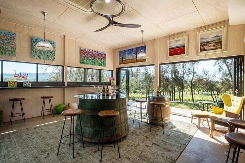 A modern kitchen with a bar area, wooden stools, a large window overlooking a garden, and artwork on the walls. 5