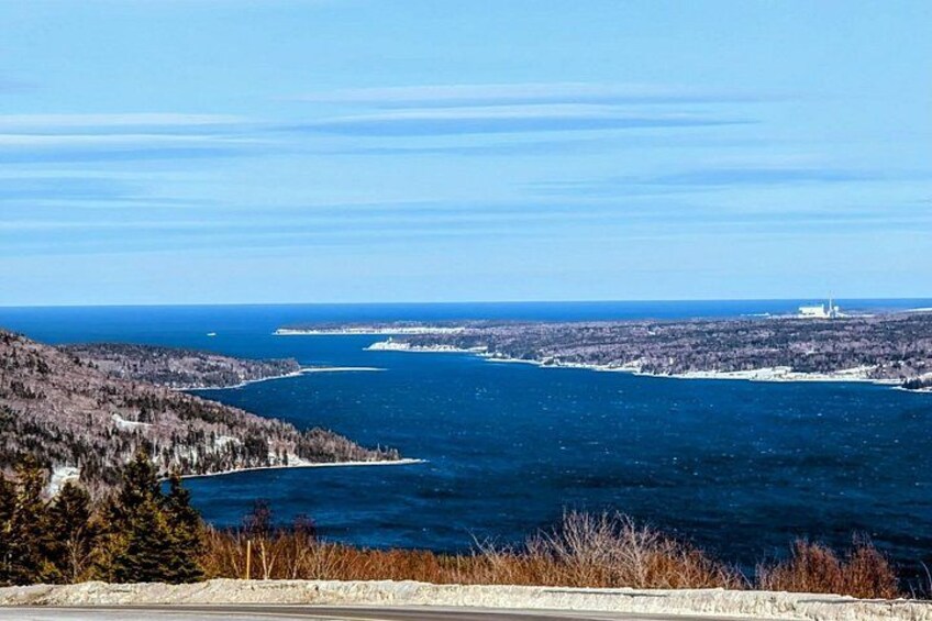 A coastal landscape with a clear sky, a large body of water, and a distant shoreline with buildings. 4
