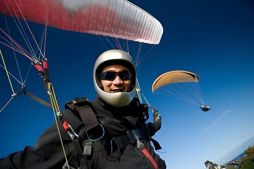 A person paragliding with a parachute, another paraglider in the background, and a clear blue sky. 4