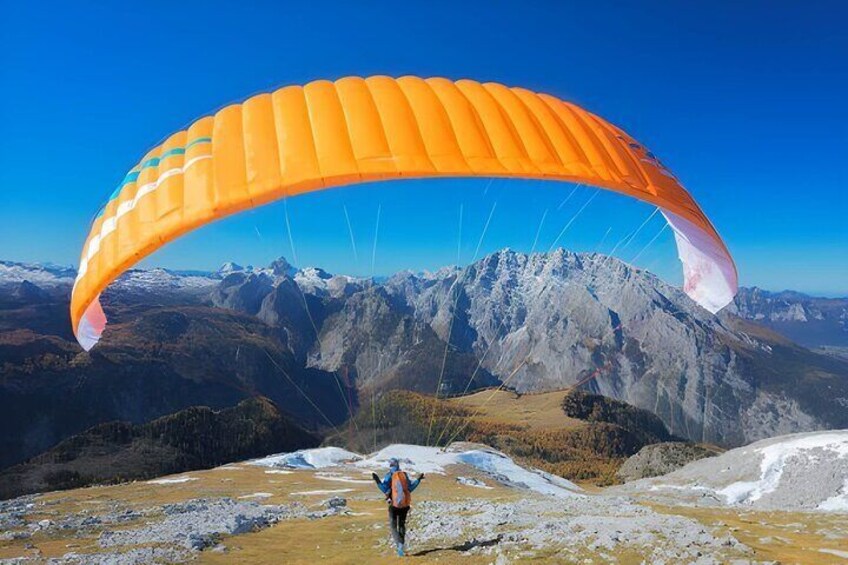 A person paragliding over a mountainous landscape with snow-capped peaks and a clear blue sky. 1