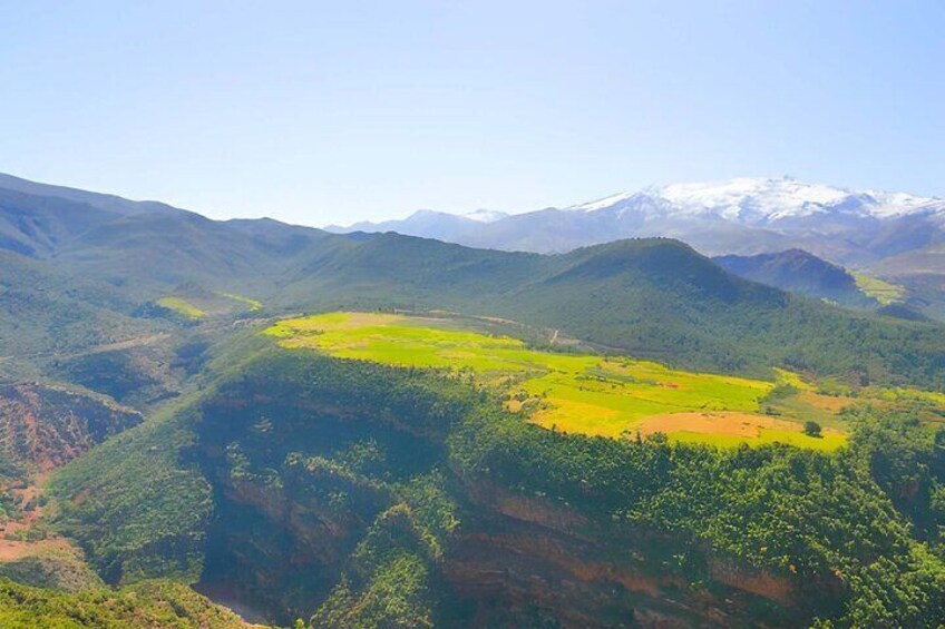 A mountainous landscape with a valley, green fields, and snow-capped peaks in the distance. 2