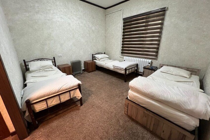 A room with three wooden beds, a radiator, and a window with blinds. 4