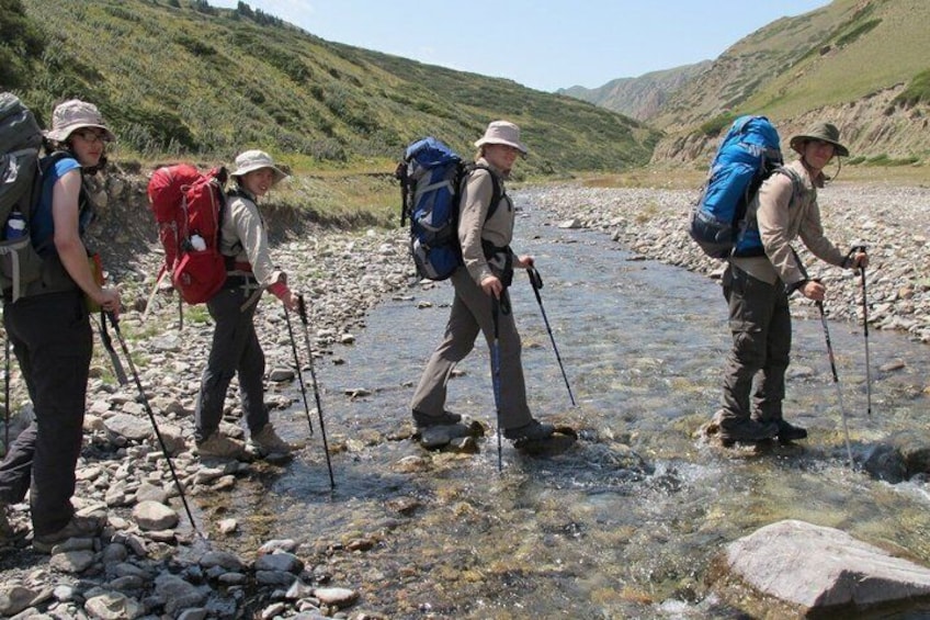 Hikers crossing a shallow stream with backpacks and trekking poles. 1