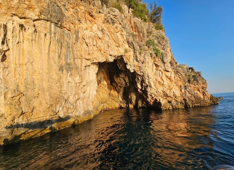A rocky coastline with a cave entrance and clear blue water. 3