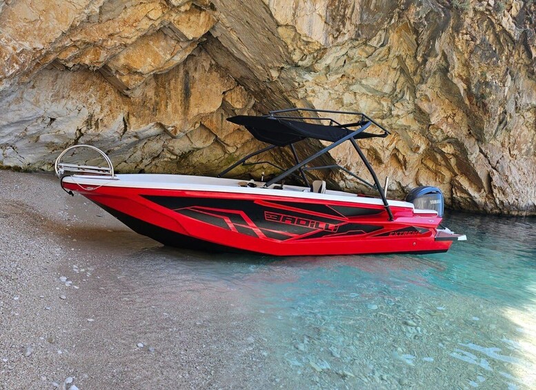 A red and white speedboat with a Yamaha engine, docked near a rocky shoreline. 1