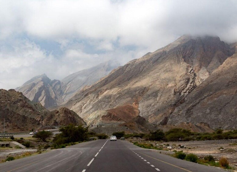 A road flanked by rugged mountains with a vehicle in the distance. 1